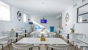 A modern dining area with white tables and chairs, a television screen, and decorative wall art. - Hostal La Isla (Carboneras)