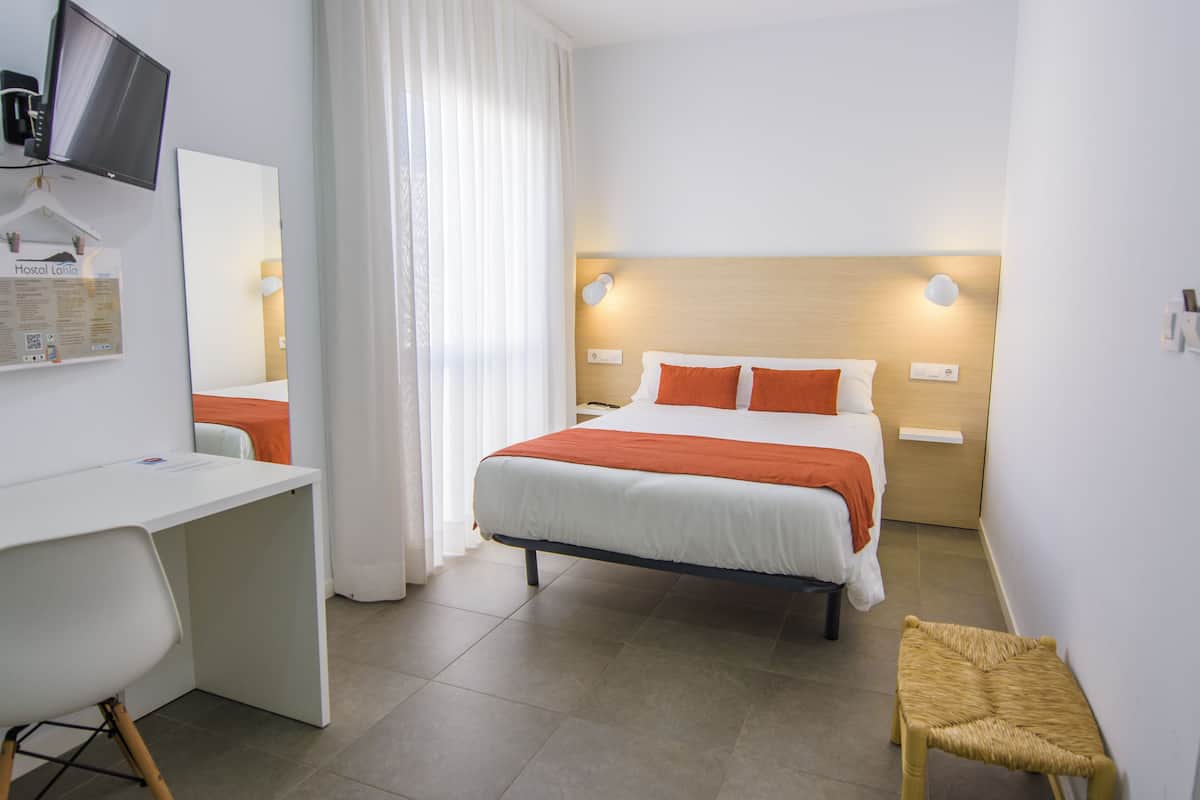 A hotel room with a bed, a desk, a chair, a television, and a small table.