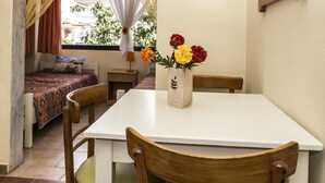 Una habitación con una cama, una mesa con sillas, un florero con flores y una ventana con cortinas.