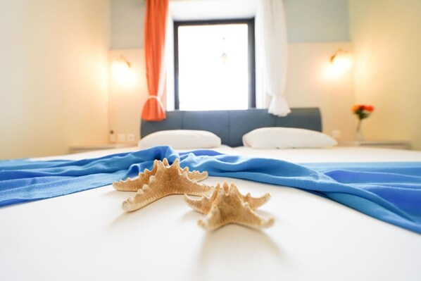 Habitación de hotel con cama, dos caracoles sobre la cama, una manta azul y una ventana con cortinas.