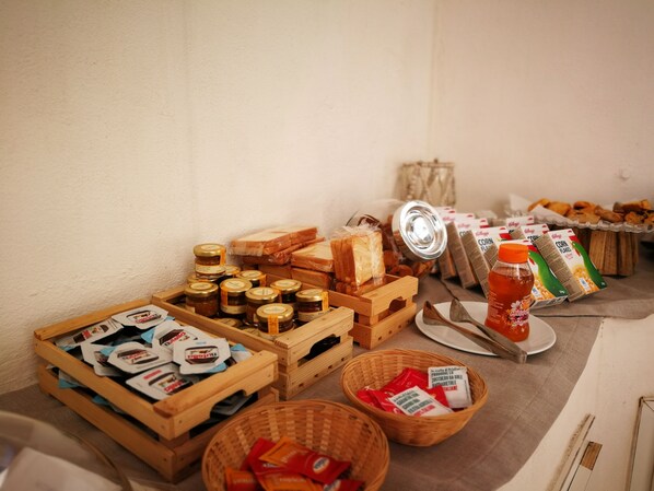 Una mesa de buffet con diferentes alimentos, incluyendo frascos de conservas, pan, cajas de cereales y salsas.
