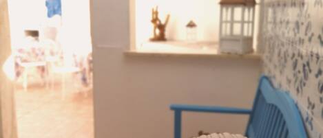 Una habitación con una mesa de madera, una silla azul, una pared con letrero de no fumar y vistas a un espacio exterior con una silla y una estructura pequeña.