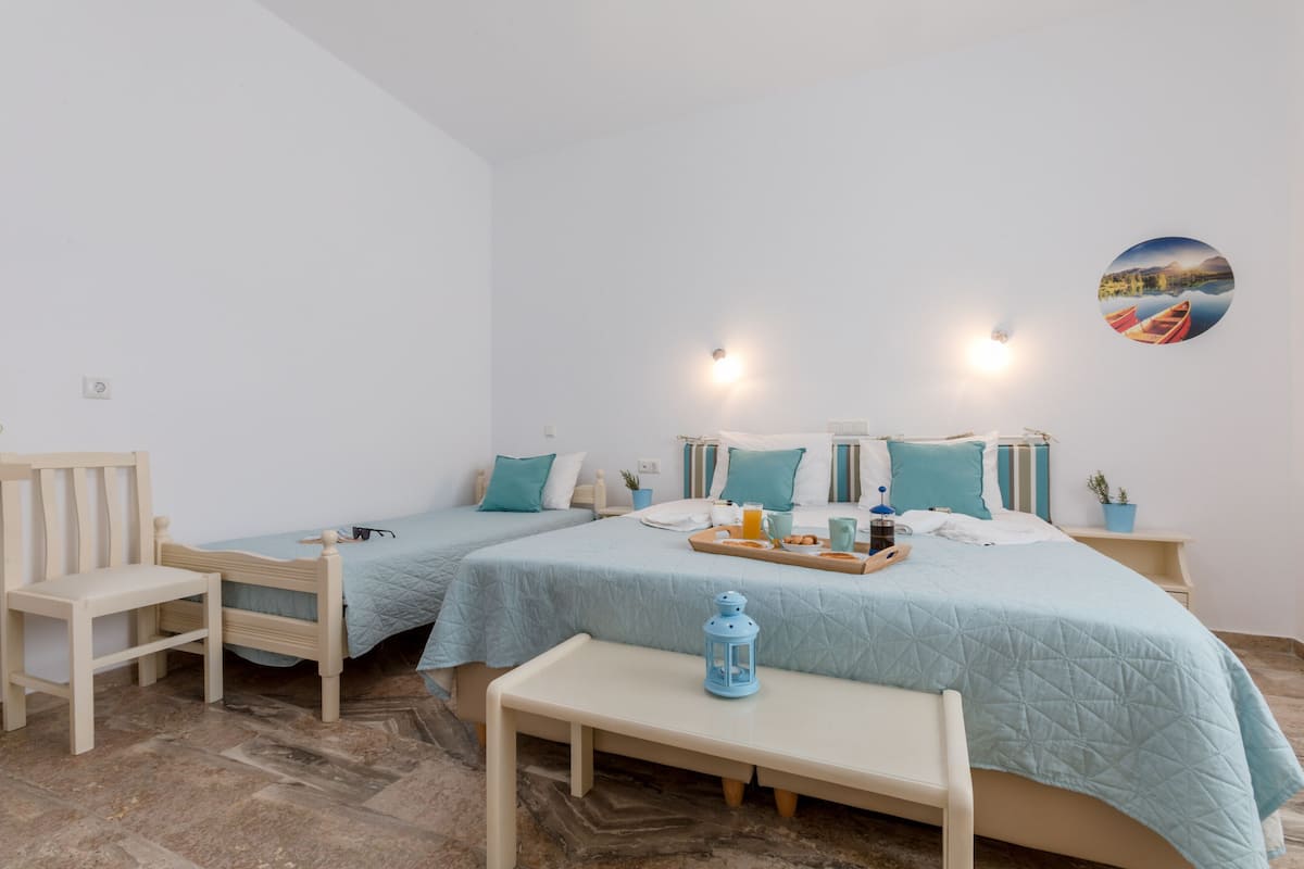 A bedroom with two beds, a bench, a table, and a wall-mounted picture.