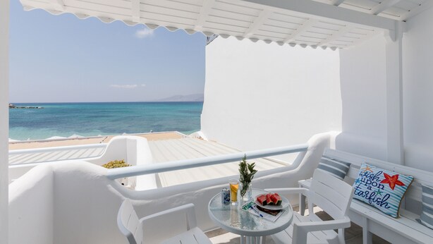 Un balcon blanc avec une table, des chaises et une vue sur la mer.