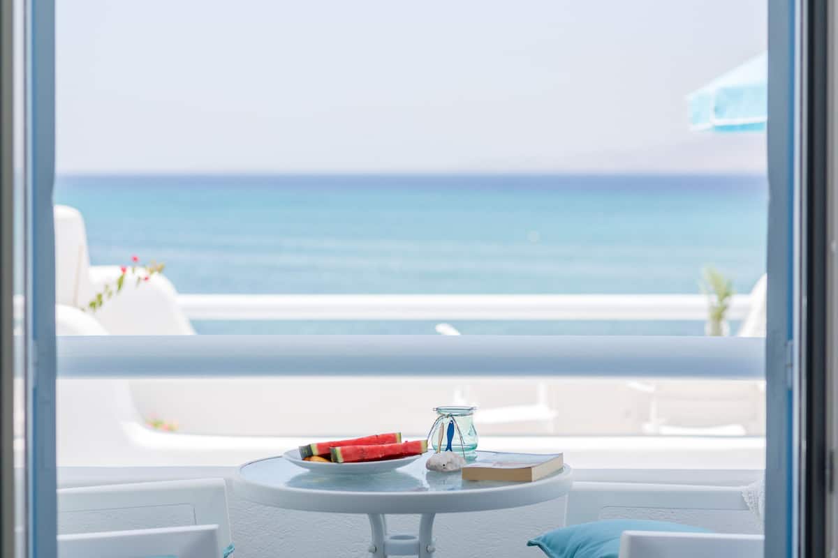 A balcony with a view of the sea, a small table with a book, a glass jar, and a plate with food.