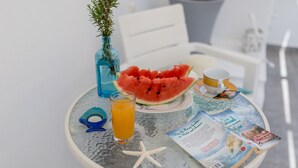 Une table avec un verre de jus d’orange, une tranche de pastèque, une étoile de mer, une brochure et un petit vase avec une plante.