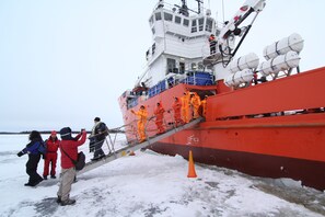Un gran barco con personas uniformadas de naranja que suben por una rampa.