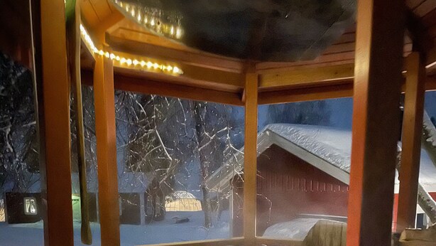 A hot tub with a wooden frame and steps leading up to it, surrounded by a snowy landscape and a wooden structure in the background. - Filipsborg, the Arctic Mansion (Kalix)