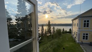 A view from a window overlooking a grassy area with a building and a body of water. - Filipsborg, the Arctic Mansion (Kalix)