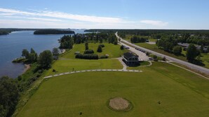 An aerial view of a golf course with a clubhouse, a parking lot, and a road running alongside. - Filipsborg, the Arctic Mansion (Kalix)