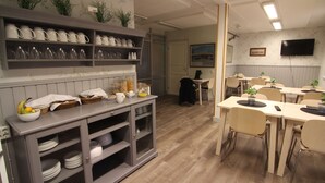 A dining area with a grey cabinet holding plates and bowls, a table with chairs, and a television mounted on the wall. - Filipsborg, the Arctic Mansion (Kalix)