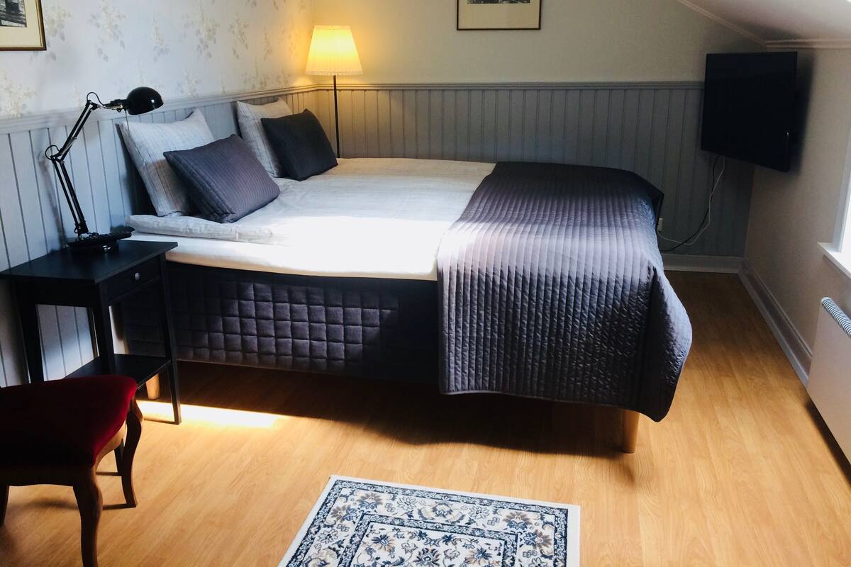 A bedroom with a bed, bedside lamp, TV, and a small table.