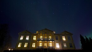 A large, yellow building with multiple windows and a balcony, illuminated at night. - Filipsborg, the Arctic Mansion (Kalix)