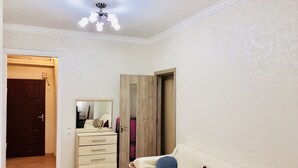 A room with a wooden floor, a white sofa with floral patterns, a mirror, and a wooden wardrobe. - Check-in apartment Metropark Mall (Baku)