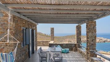Un patio de piedra con una mesa y sillas, una hamaca colgante y vistas al mar.
