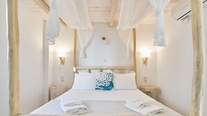 A bed with white linens, a wooden headboard, and a canopy. There are two bedside tables with lamps. - Cape Suites (Kithnos)