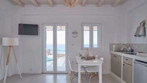 A modern kitchen with a dining area, a TV mounted on the wall, and a view of the sea through the sliding doors. - Cape Suites (Kithnos)