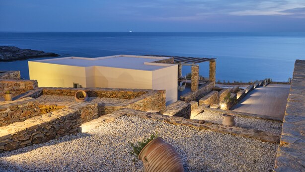 A rooftop terrace with a stone pathway, a white structure, and a view of the sea. - Cape Suites (Kithnos)