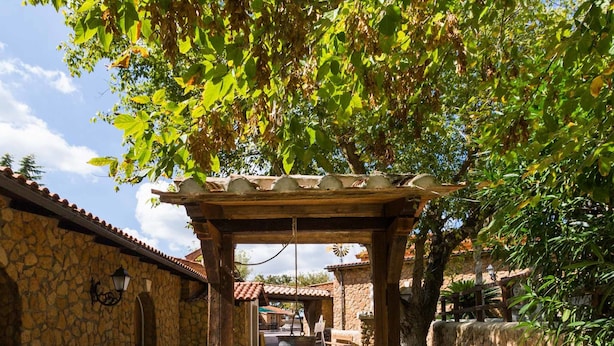 Une cour pavée de pierres, agrémentée d’une pergola en bois, de murs en pierre et d’une fontaine en pierre.