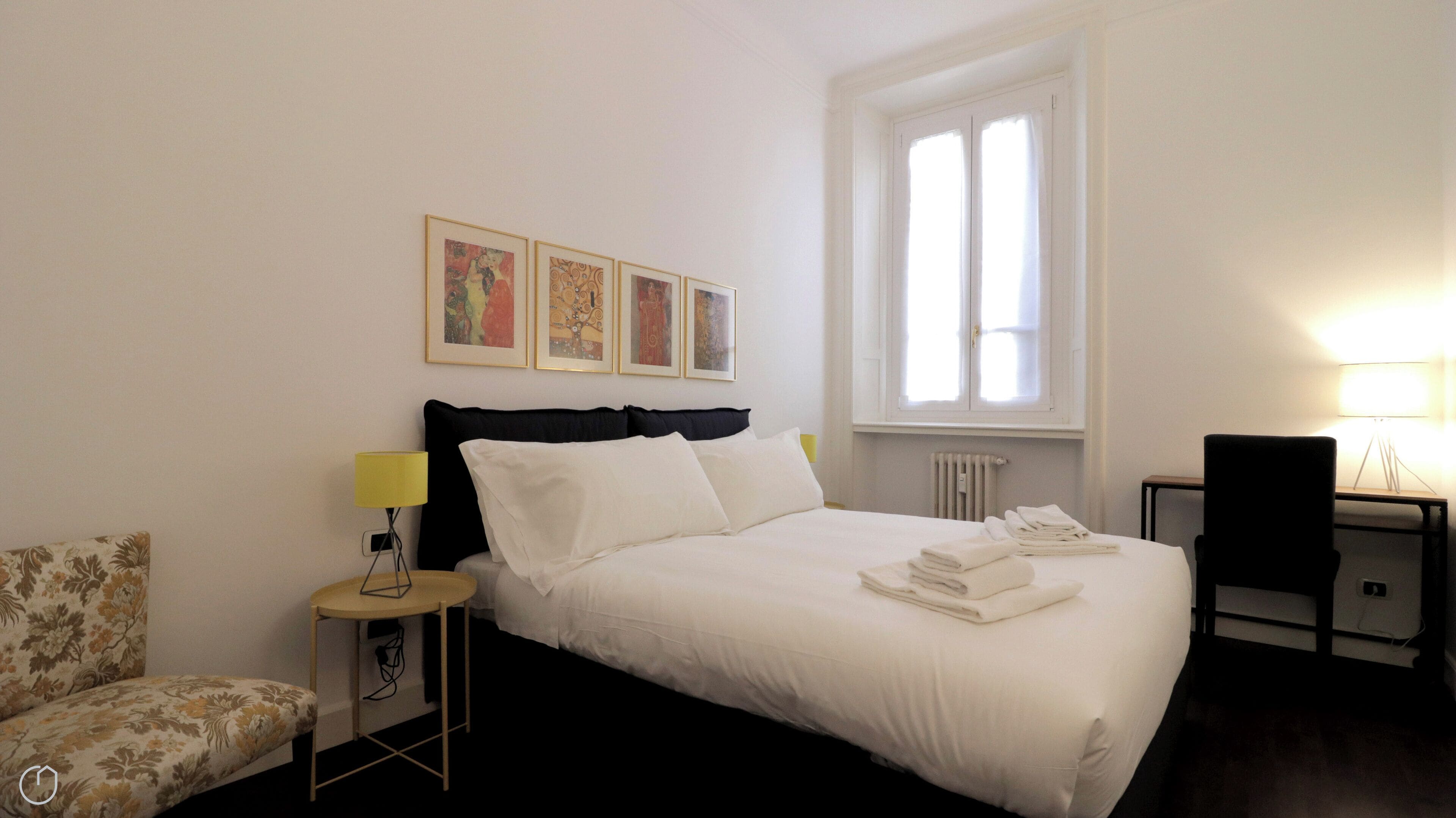 A hotel room with a bed, a chair, a small table, and a window.