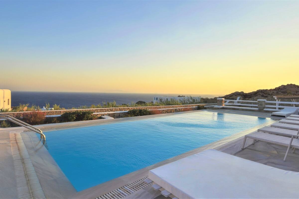 A pool with lounge chairs and a view of the sea.
