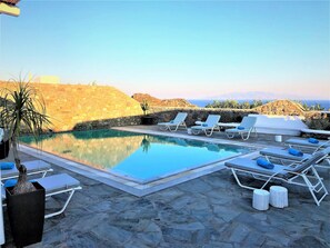 A pool area with lounge chairs and a view of the sea.