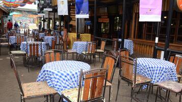 An outdoor cafe with tables covered in blue and white checkered tablecloths, wooden chairs, and hanging decorations.