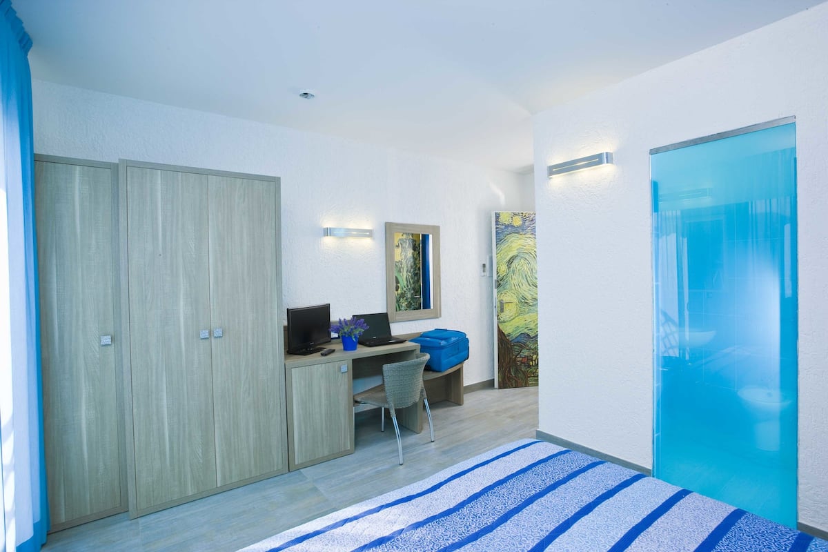 A modern bedroom with a bed, a desk with a laptop, a chair, and a wardrobe.