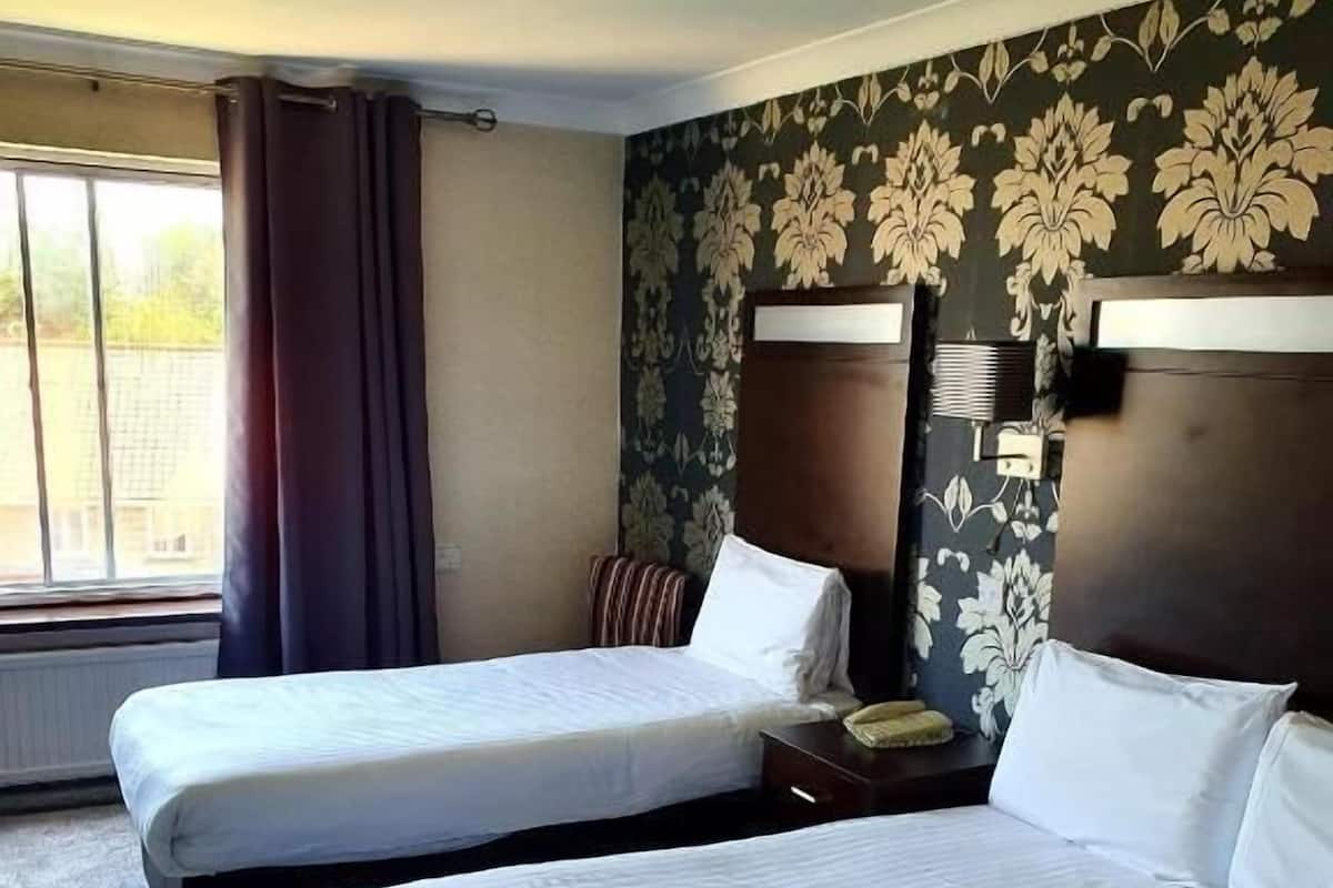 Ett hotellrum med två separata sängar, en stor säng, ett fönster med gardiner och en tapet med blommönster.