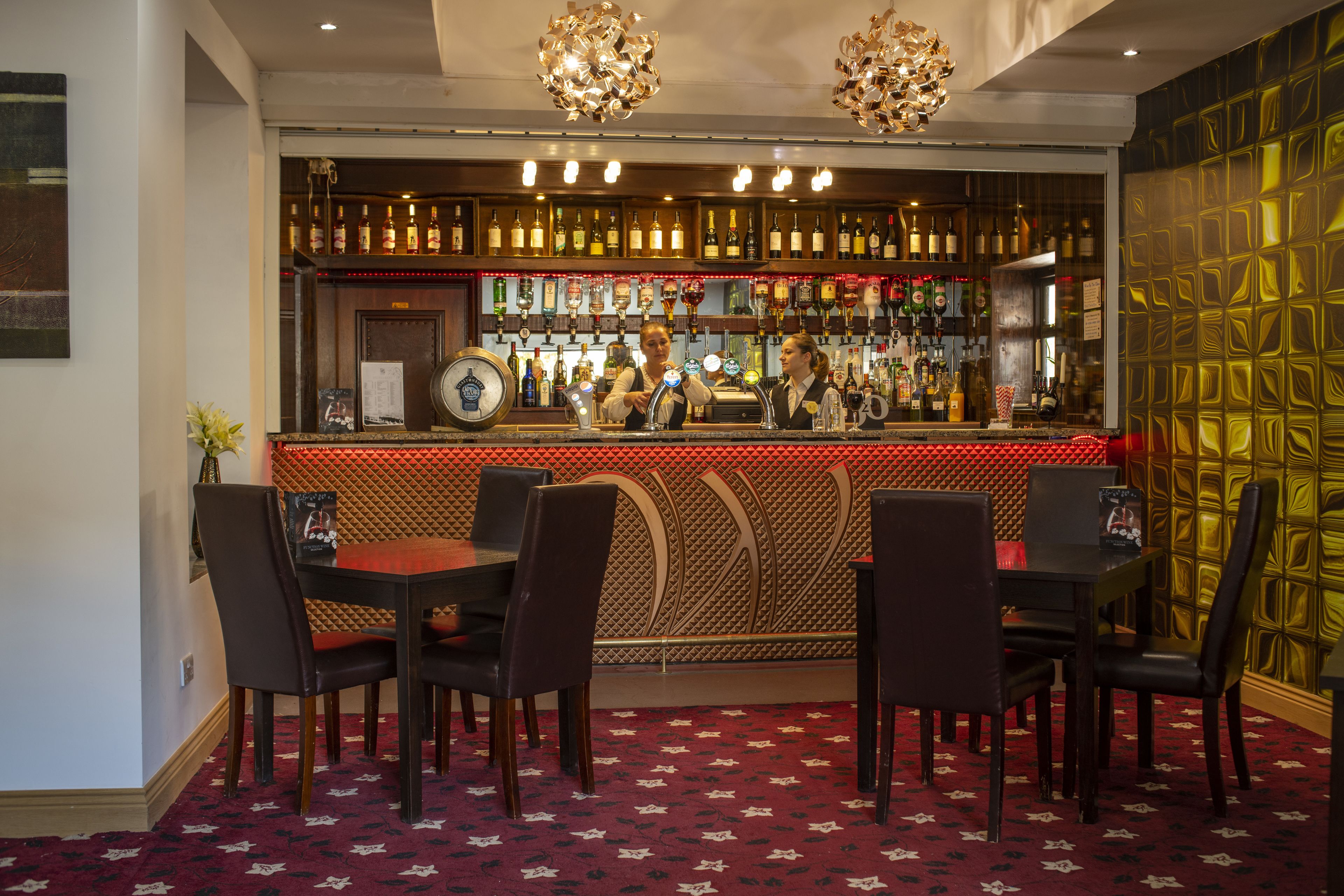 A bar area with a counter, bar stools, and a variety of bottles. There are two barbacks behind the counter.