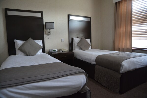 A hotel room with two single beds, each with a pillow and a bedside table. - Wessex Hotel (Street)