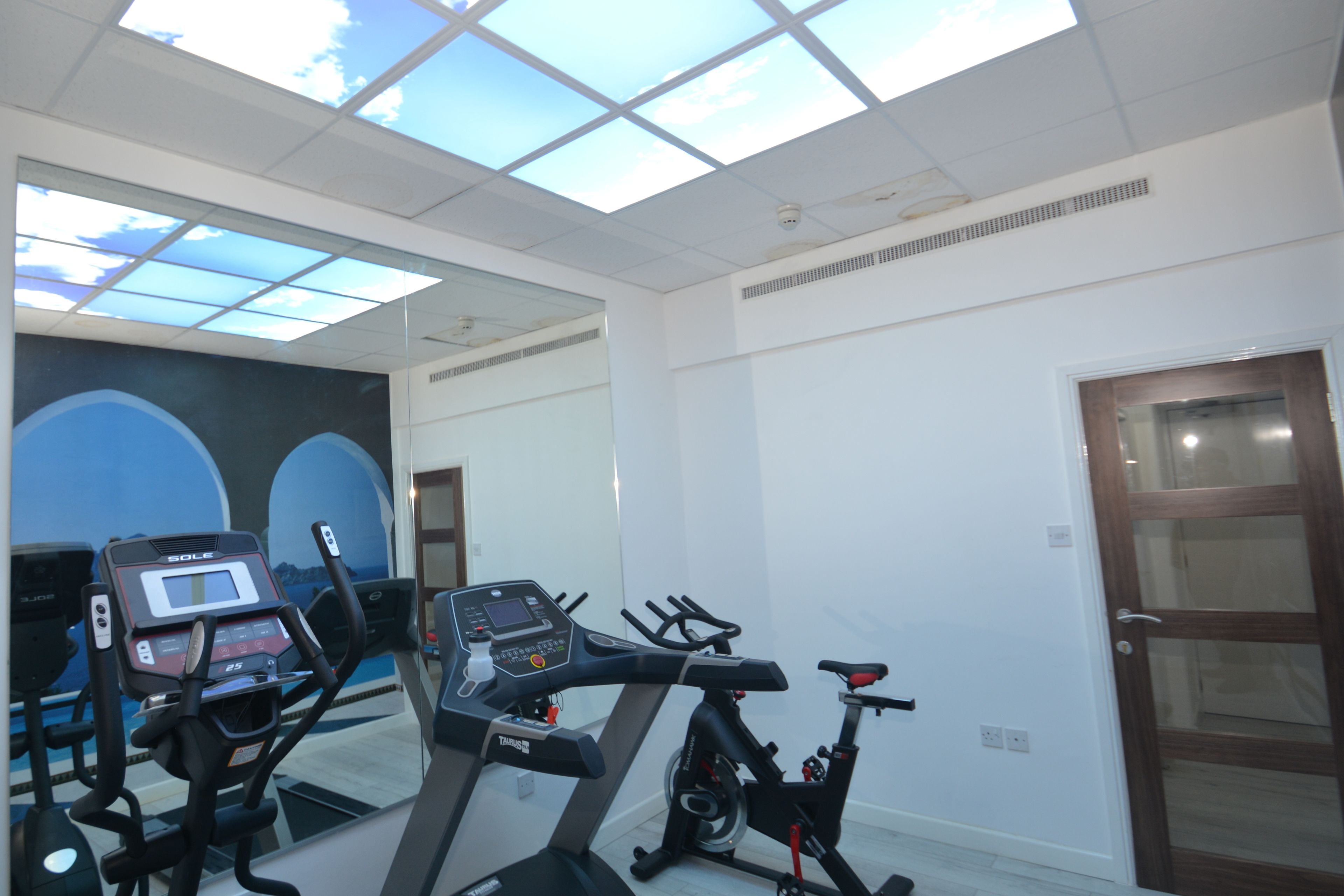 Een sportschool met trainingsapparatuur, een groot raam en een deur.