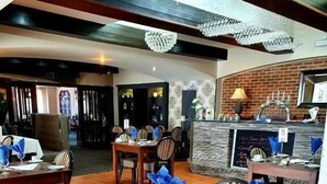 A dining area with wooden tables and striped chairs, a brick wall, and a bar area with a chalkboard menu. - Wessex Hotel (Street)