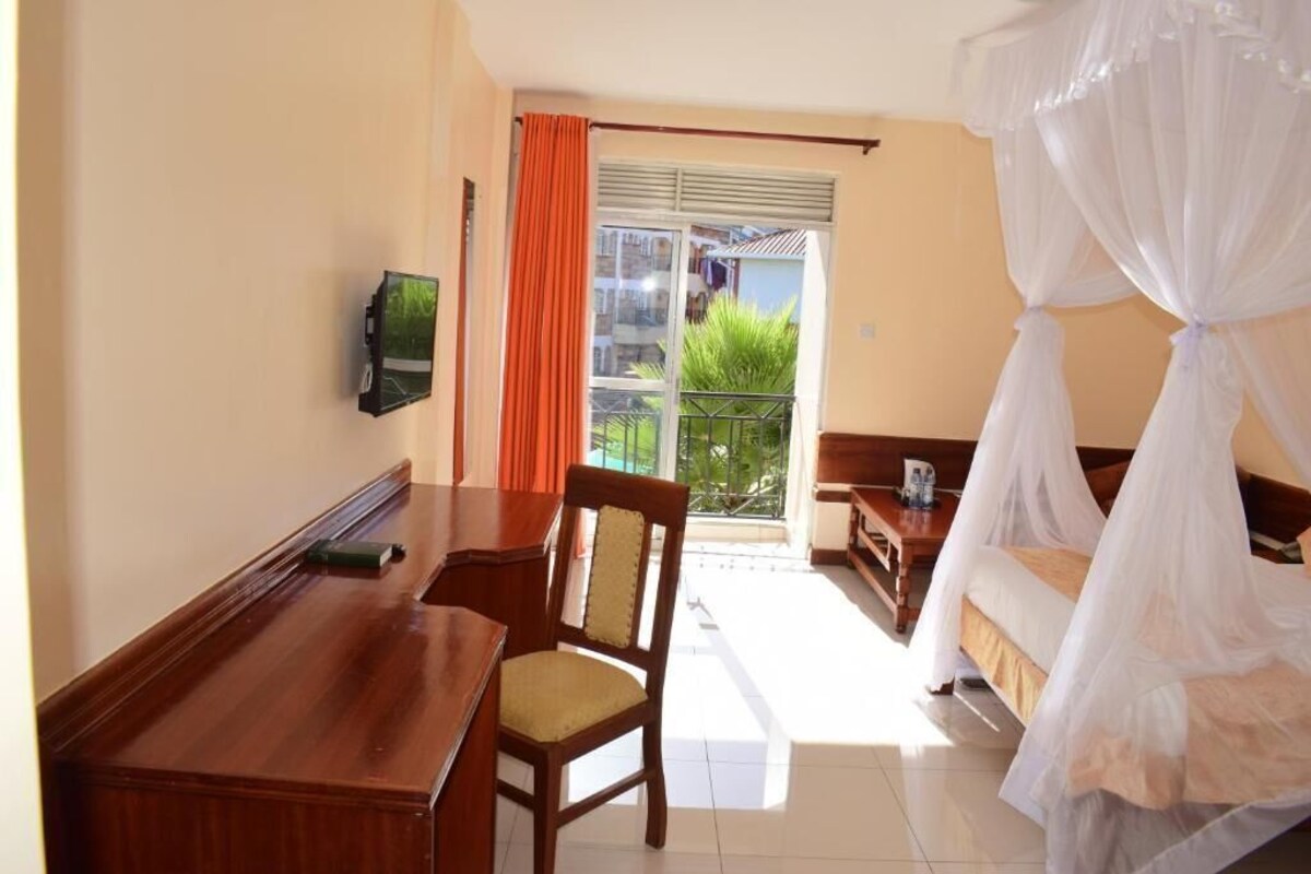 Habitación de hotel con cama, escritorio, silla, televisión y balcón con vistas.