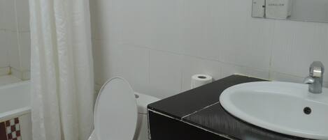 Un baño con inodoro blanco, lavamanos negro, espejo y cortina de ducha.