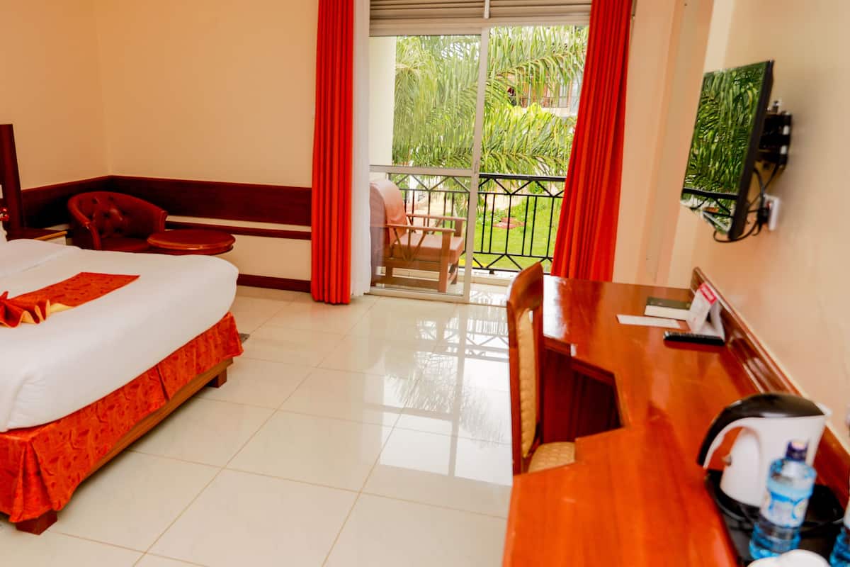 Habitación de hotel con cama, escritorio, silla, televisión y balcón con vistas a la vegetación.