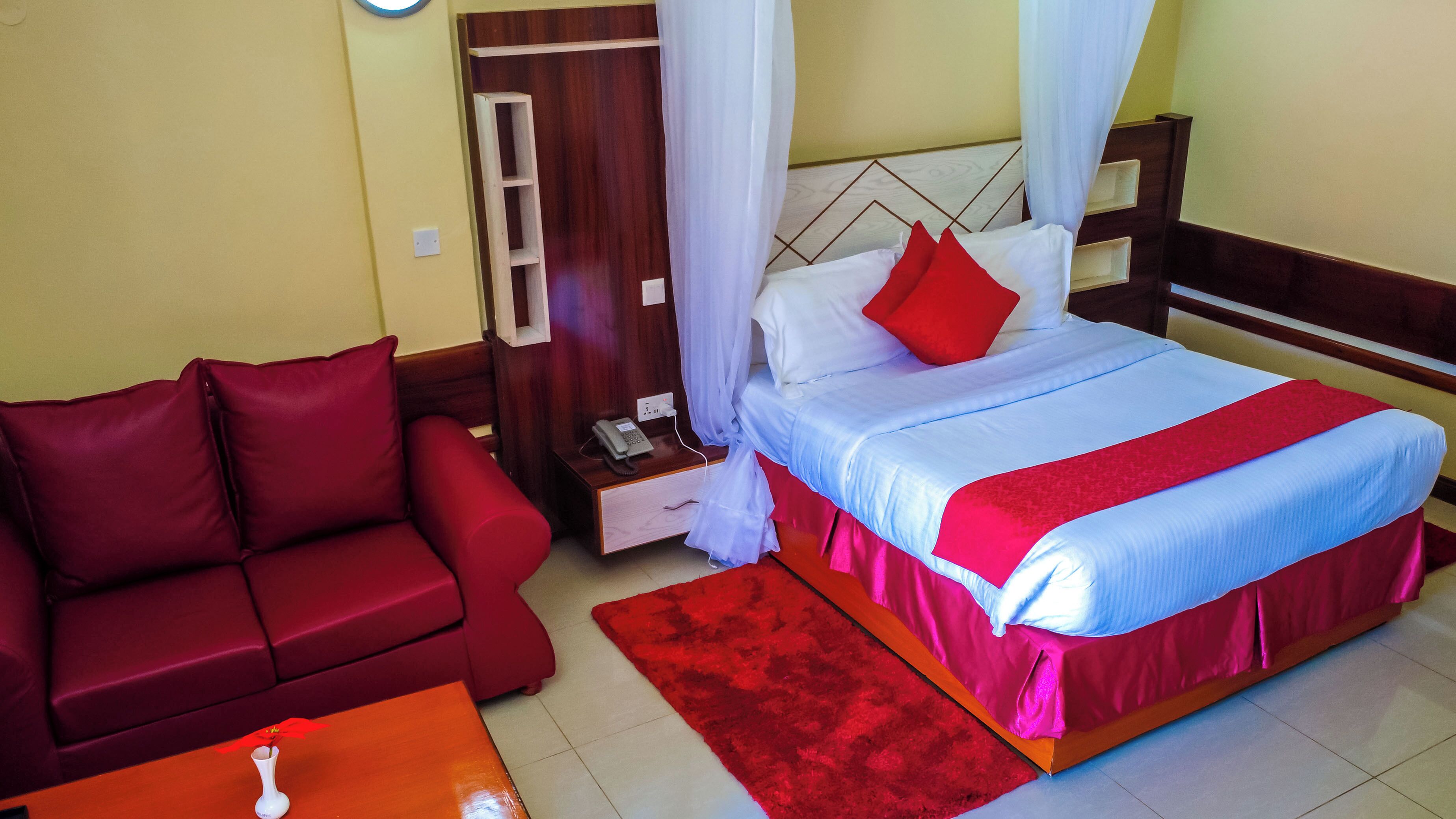 Una habitación de hotel con una cama, un sofá rojo, una mesita de noche con un teléfono y una alfombra roja.