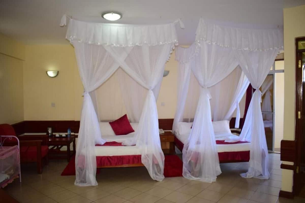 Una habitación con dos camas, cada una con dosel, un sofá, una mesa y una lámpara de pared.