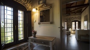 Een kamer met een stenen muur, een houten bank, een bureau met lades en een grote spiegel.