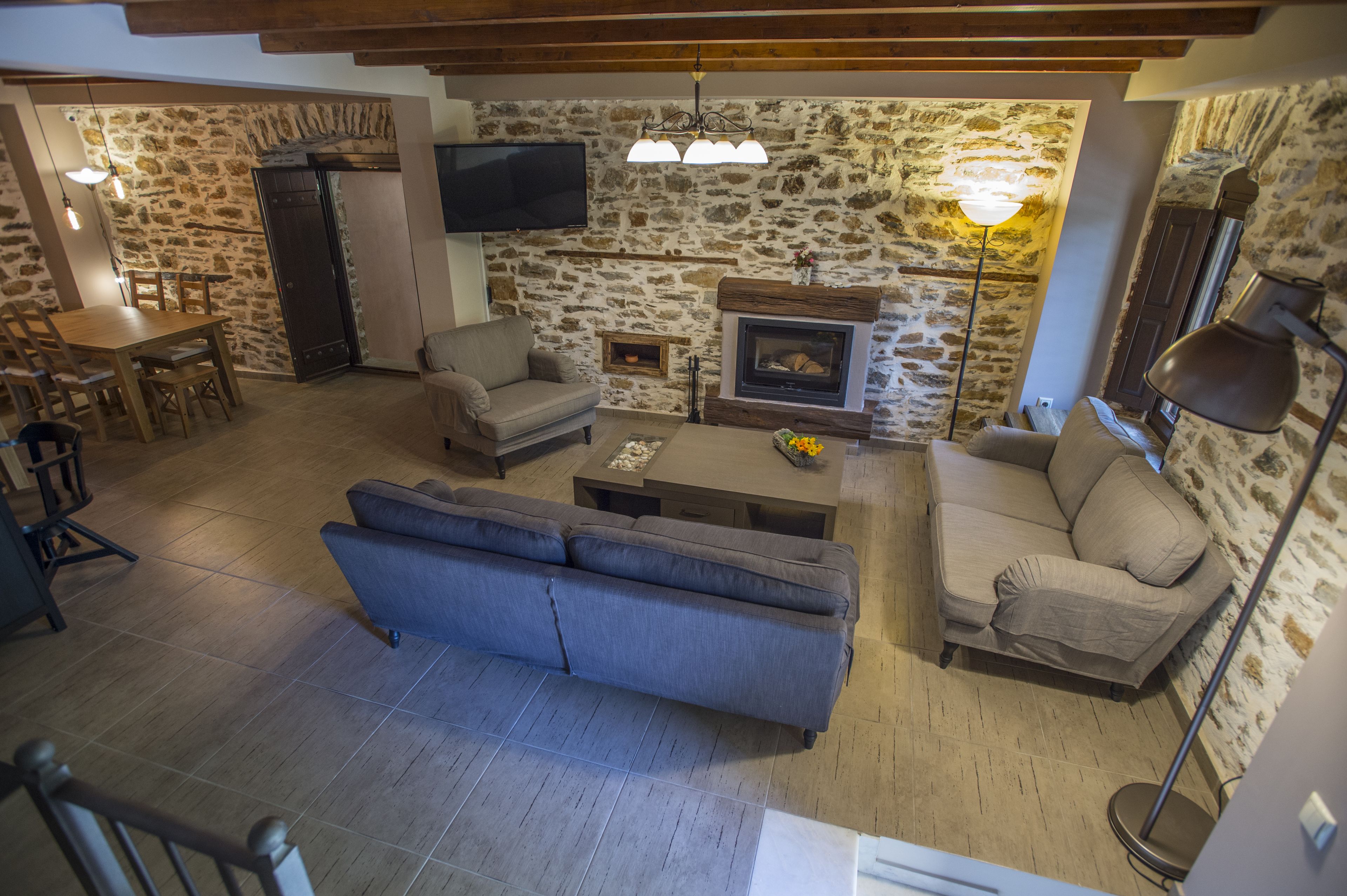 A cozy living room with a stone wall, a fireplace, a sofa, a coffee table, and a TV mounted on the wall.