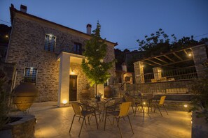 Un bâtiment en pierre doté d’un patio aménagé avec des sièges extérieurs et un arbre.