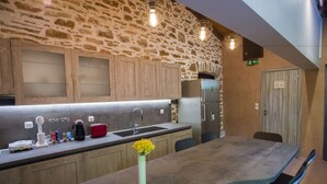 Een moderne keuken met een stenen muur, houten kasten, een roestvrijstalen koelkast en een lange eettafel met stoelen.