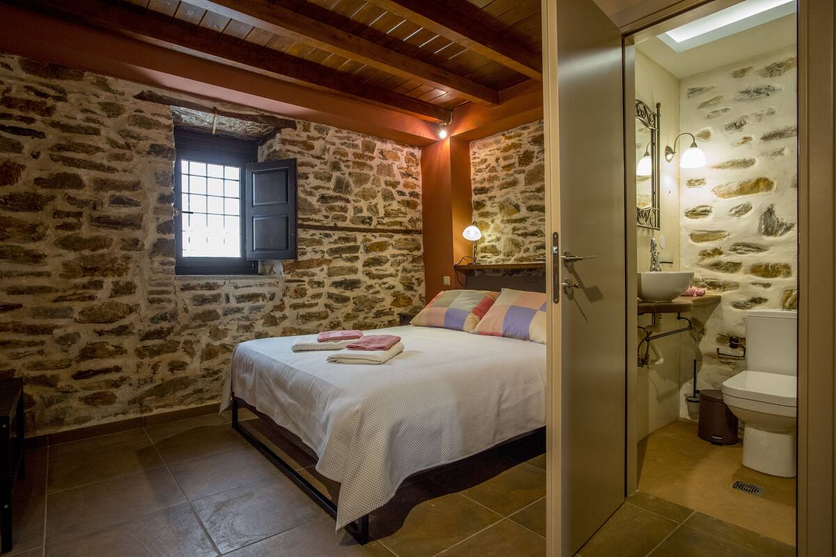 Ein Schlafzimmer mit Steinsturz, einem Bett mit Kissen, einem Fenster und einem Badezimmer mit Steinsturz und Waschbecken.