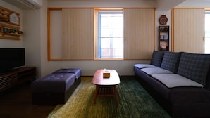 A living room with a sofa, a small table, a TV, and a window with wooden blinds. - Rooms (Tokyo)