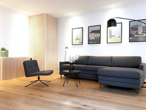 A modern living room with a grey sectional sofa, a black office chair, a small round table with a vase, and a tall floor lamp. - The Nordic Collection VIII (Copenhagen)