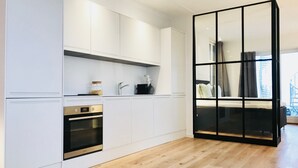 Una cocina moderna con muebles blancos, un horno empotrado y una puerta corredera de marco negro que da a un dormitorio.