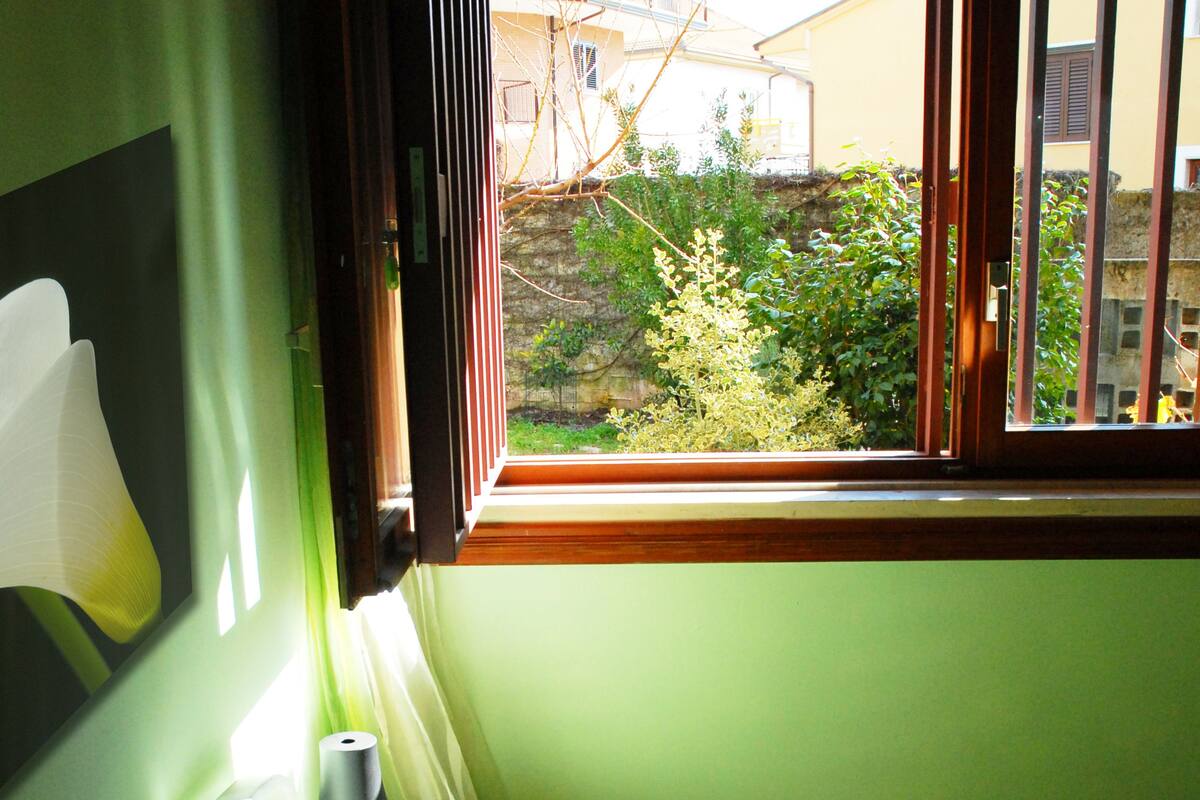 A room with a bed, a window, and a view of greenery outside.