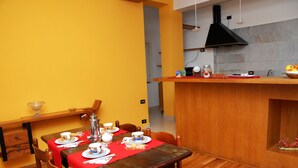 Ein Essbereich mit einem Holztisch, gedeckt für vier Personen, einer roten Tischdecke und einer Küchenzeile mit einer schwarzen Dunstabzugshaube.