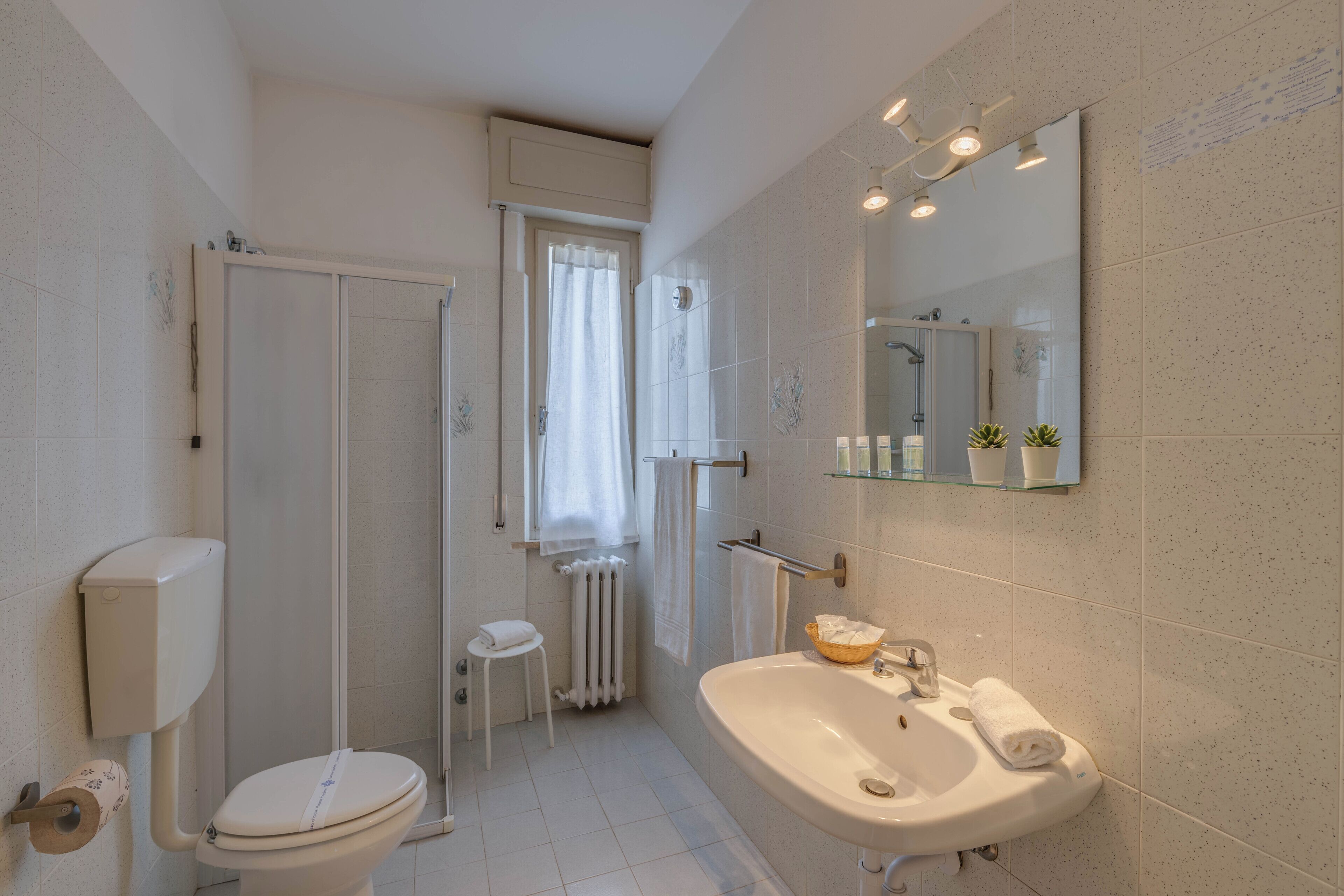 A bathroom with a toilet, sink, shower, and a mirror.
