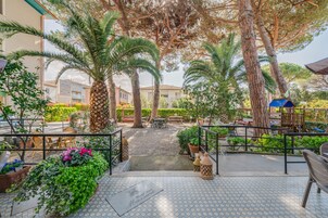 Un patio de hotel con mobiliario exterior, palmeras y suelo de baldosas.